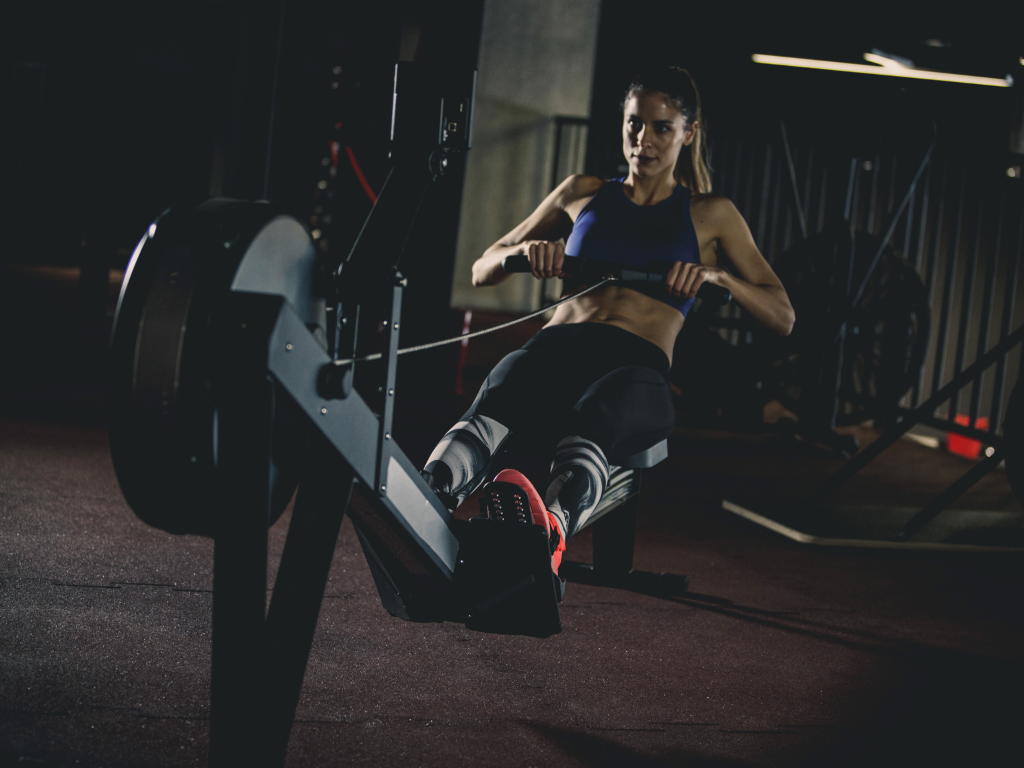 A woman mid-drive on a Concept2 RowErg in a dark gym