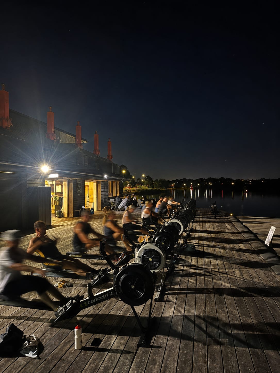 A Row Club crew training on RowErgs along the boatshed pontoon at dusk